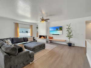 Living room featuring ceiling fan, a textured ceiling, and light hardwood / wood-style floors