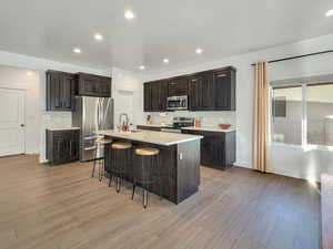 Kitchen with a textured ceiling, a kitchen island with sink, appliances with stainless steel finishes, a breakfast bar, and light hardwood / wood-style floors