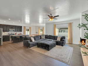 Living room with ceiling fan, a textured ceiling, and light hardwood / wood-style flooring