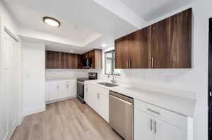 Kitchen with light hardwood / wood-style floors, dark brown cabinetry, sink, stainless steel appliances, and white cabinets