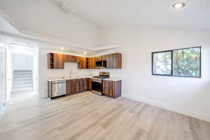 Kitchen featuring appliances with stainless steel finishes, high vaulted ceiling, sink, and light hardwood / wood-style floors