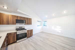 Kitchen with lofted ceiling, light hardwood / wood-style floors, appliances with stainless steel finishes, and a textured ceiling