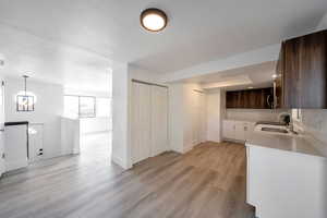 Kitchen with dark brown cabinetry, sink, light hardwood / wood-style floors, decorative light fixtures, and a textured ceiling