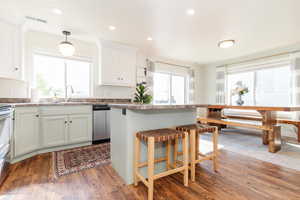 Kitchen featuring a breakfast bar, dark wood-type flooring, sink, dishwasher, and hanging light fixtures