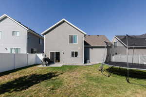 Rear view of house with central AC unit, a trampoline, a yard, and a patio