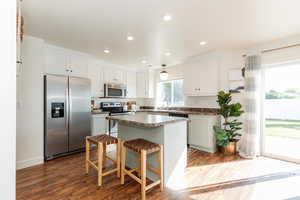 Kitchen with a breakfast bar area, dark wood-type flooring, stainless steel appliances, a center island, and white cabinetry