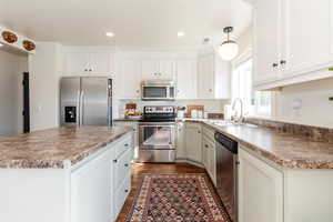 Kitchen with appliances with stainless steel finishes, hanging light fixtures, sink, and white cabinetry