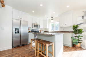 Kitchen featuring a kitchen island, a breakfast bar, dark hardwood / wood-style floors, appliances with stainless steel finishes, and white cabinetry