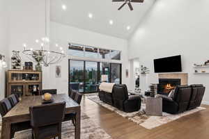 Dining space featuring ceiling fan with notable chandelier, high vaulted ceiling, a fireplace, and hardwood / wood-style floors