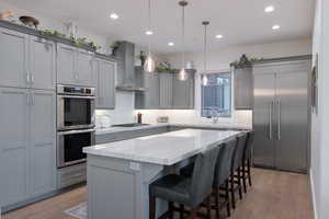 Kitchen featuring hardwood / wood-style floors, a center island, stainless steel appliances, wall chimney exhaust hood, and pendant lighting