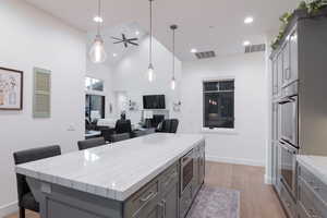 Kitchen featuring light hardwood / wood-style floors, gray cabinets, a kitchen island, light stone counters, and high vaulted ceiling