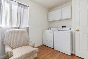 Laundry area with washing machine and dryer, cabinets, and light hardwood / wood-style flooring