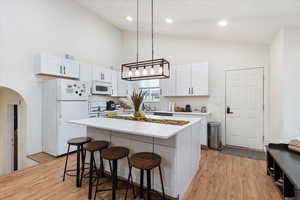 Kitchen featuring a kitchen island, white appliances, light hardwood / wood-style floors, hanging light fixtures, and white cabinetry