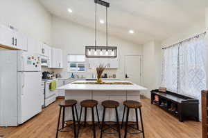 Kitchen featuring hanging light fixtures, white appliances, light hardwood / wood-style flooring, a center island, and a breakfast bar