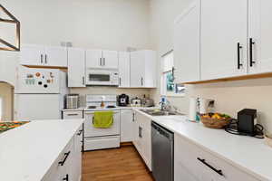 Kitchen with light hardwood / wood-style flooring, white appliances, sink, and white cabinetry