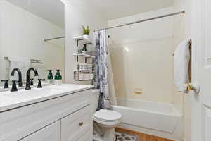 Full bathroom featuring hardwood / wood-style floors, shower / bath combination with curtain, vanity, and toilet