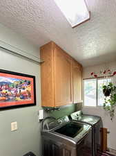 Washroom featuring washer and dryer, cabinets, a skylight, and a textured ceiling