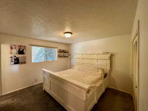 Bedroom featuring a textured ceiling, a closet, and dark colored carpet