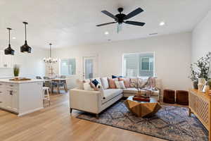 Living room with ceiling fan with notable chandelier and light hardwood / wood-style floors