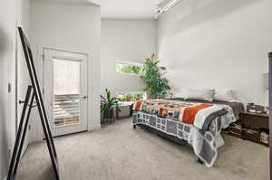 Bedroom featuring light carpet, a towering ceiling, and access to exterior