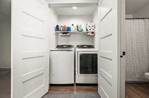 Clothes washing area with dark hardwood / wood-style flooring and washing machine and clothes dryer