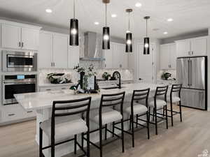 Kitchen featuring wall chimney exhaust hood, white cabinets, appliances with stainless steel finishes, and a kitchen island with sink