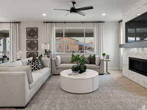 Living room with ceiling fan, light wood-type flooring, and a high end fireplace