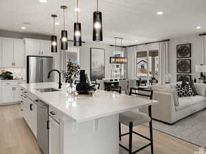 Kitchen with light hardwood / wood-style flooring, hanging light fixtures, white cabinets, appliances with stainless steel finishes, and an island with sink