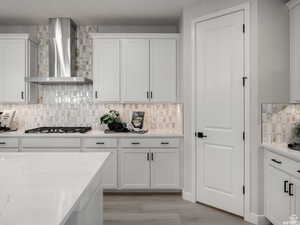 Kitchen with wall chimney range hood, stainless steel gas stovetop, and white cabinetry