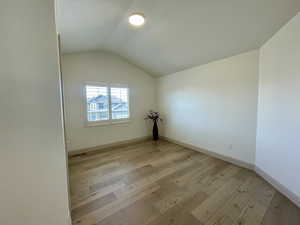 Unfurnished room featuring light wood-type flooring and vaulted ceiling