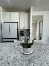 Kitchen with decorative backsplash, white cabinets, white fridge, and light stone counters