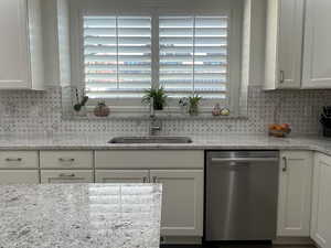 Kitchen with dishwasher, light stone countertops, white cabinets, and sink