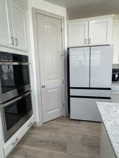 Kitchen featuring light hardwood / wood-style flooring, light stone countertops, double oven, white fridge, and white cabinetry