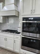 Kitchen with light wood-type flooring, light stone countertops, premium range hood, white cabinetry, and appliances with stainless steel finishes