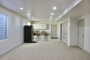 Kitchen featuring a center island, white cabinets, stainless steel refrigerator, a kitchen bar, and light colored carpet