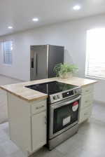 Kitchen featuring butcher block countertops, stainless steel appliances, light tile patterned floors, and a center island