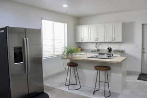 Kitchen with a kitchen island, sink, butcher block counters, white cabinets, and stainless steel refrigerator with ice dispenser