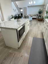 Kitchen featuring light wood-type flooring, a kitchen island, stainless steel microwave, hanging light fixtures, and white cabinets