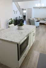 Kitchen with pendant lighting, light hardwood / wood-style flooring, white cabinetry, a center island, and a notable chandelier