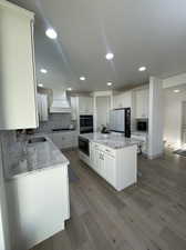 Kitchen featuring fridge, custom exhaust hood, light stone countertops, a center island, and white cabinetry