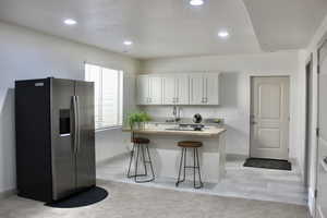 Kitchen featuring wooden counters, light colored carpet, a breakfast bar, white cabinets, and stainless steel refrigerator with ice dispenser