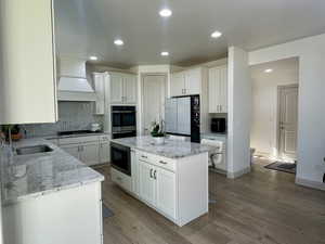 Kitchen with white cabinets, light hardwood / wood-style flooring, stainless steel appliances, and custom exhaust hood