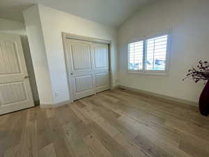 Unfurnished bedroom featuring lofted ceiling, a closet, and light wood-type flooring