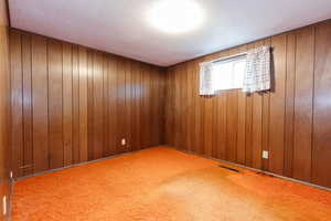 Empty room with wood walls, carpet, and a textured ceiling