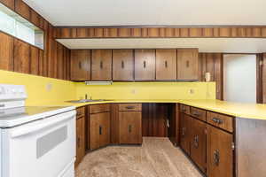 Kitchen with light carpet, white electric range, wooden walls, and sink