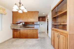 Kitchen featuring tasteful backsplash, white appliances, sink, kitchen peninsula, and a chandelier