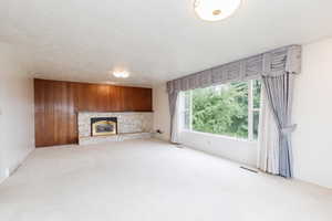 Unfurnished living room with light carpet, a textured ceiling, wooden walls, and a fireplace