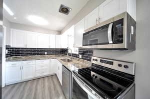 Kitchen featuring light flooring, stainless steel appliances, sink, white cabinetry, and granite counters