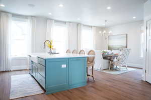 Kitchen with an island with sink, dark wood-type flooring, and a healthy amount of sunlight