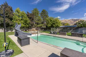 View of pool with a water slide, a patio, a yard, and a mountain view